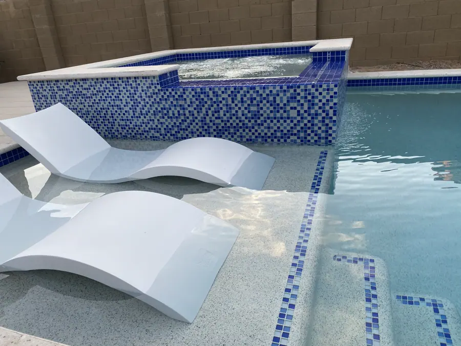 White loungers in a shallow pool shelf beside a blue-tiled spa