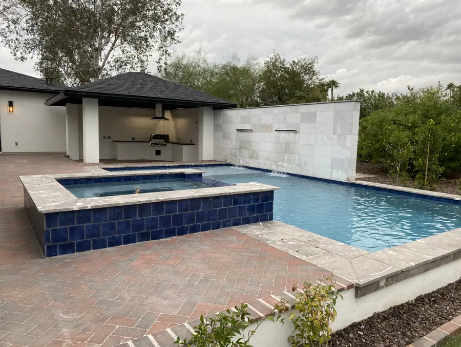 Blue-tiled raised spa beside a pool and covered outdoor kitchen