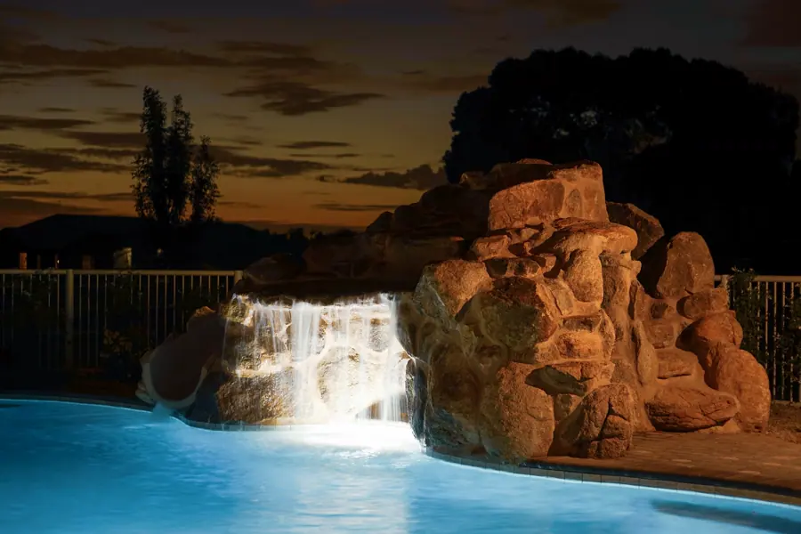 Rock waterfall lit above blue pool water at sunset