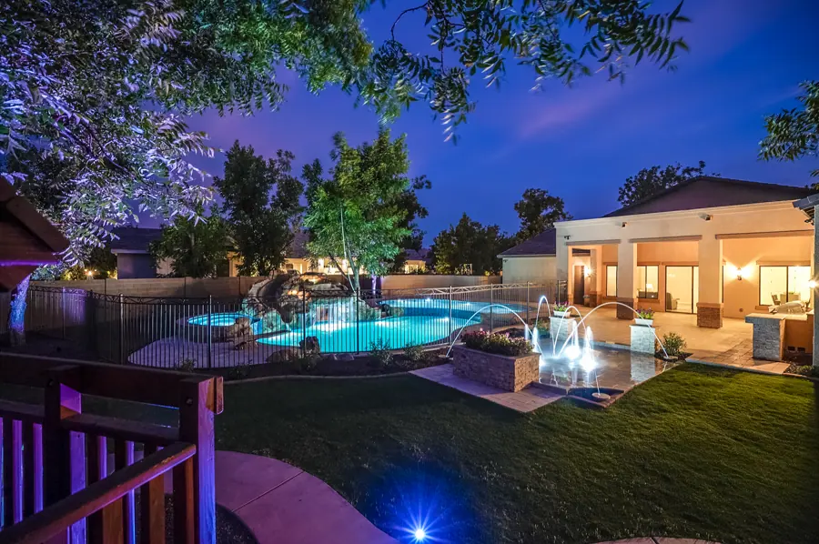 Illuminated backyard pool with water arches and colorful landscape lighting