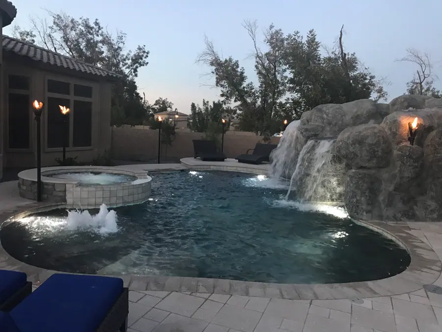Curved pool with a lit rock waterfall at dusk