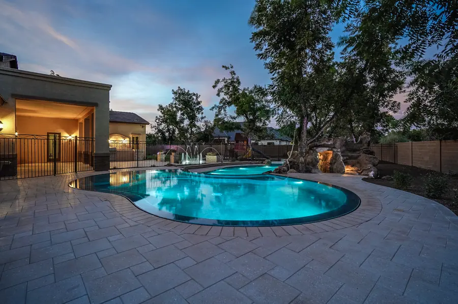 Freeform pool glowing blue beside a home at dusk
