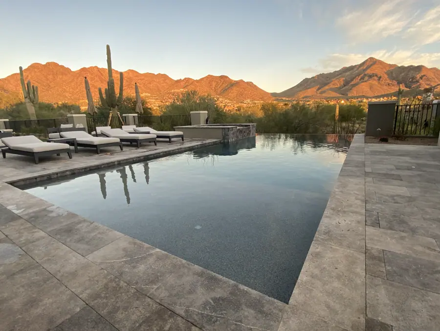 Straight-edged pool and lounge chairs facing sunlit desert mountains