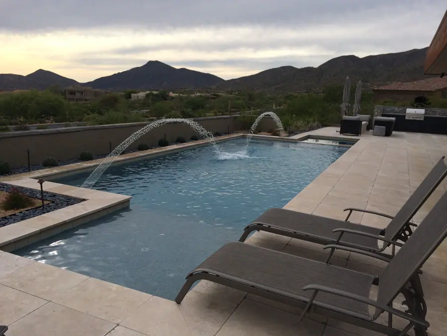 Long straight-edged pool with arcing fountains and desert hills beyond